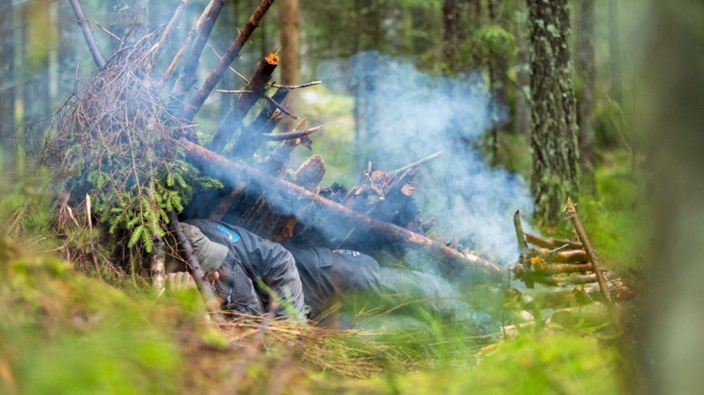 Torbjörn Selin ligger i en nödbivack med dänd eld det ryker från elden skogen är grön och lummig