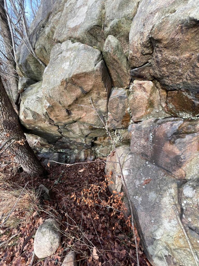 En klippa som sticker ut tillräckligt mycket för att ge en torr och regnfri plats under. Grått berg och bruna löv.