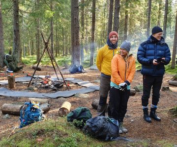 Några friluftsklädda personer står framför en eldstad förväntansfulla