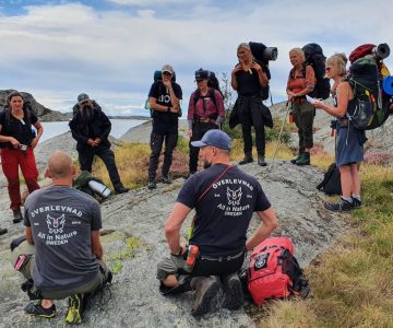 två instruktörer sitter med ryggen mot oss gruppen är samlad på en klippa framför och lyssnar på en lektion