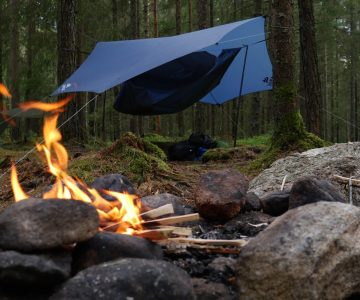 En fin lägereld i förgrunden. Längre bak hänger en hängmatta med tarp över. En del av allemansrättens rättigheter.